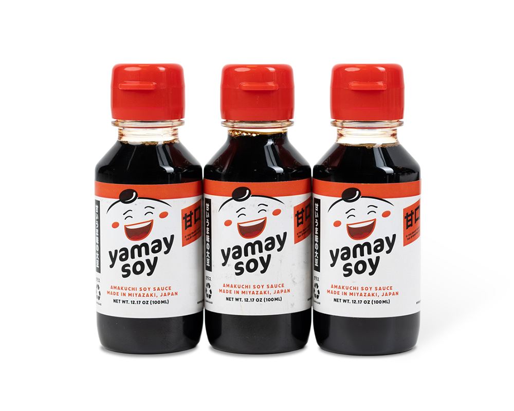 Three bottles of Yamay Soy Sauce with red caps, white labels, and a smiling face illustration on each bottle. Made in Mitzakay, Japan.
