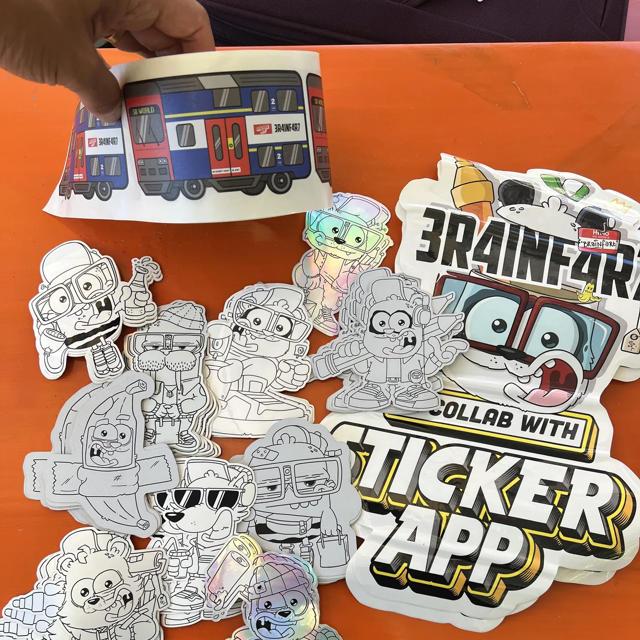 Etiket med S8 World-toget fra Brainfart x StickerApp med skiltet "In every fart is art", holdt over sort-hvide konturskårne klistermærker