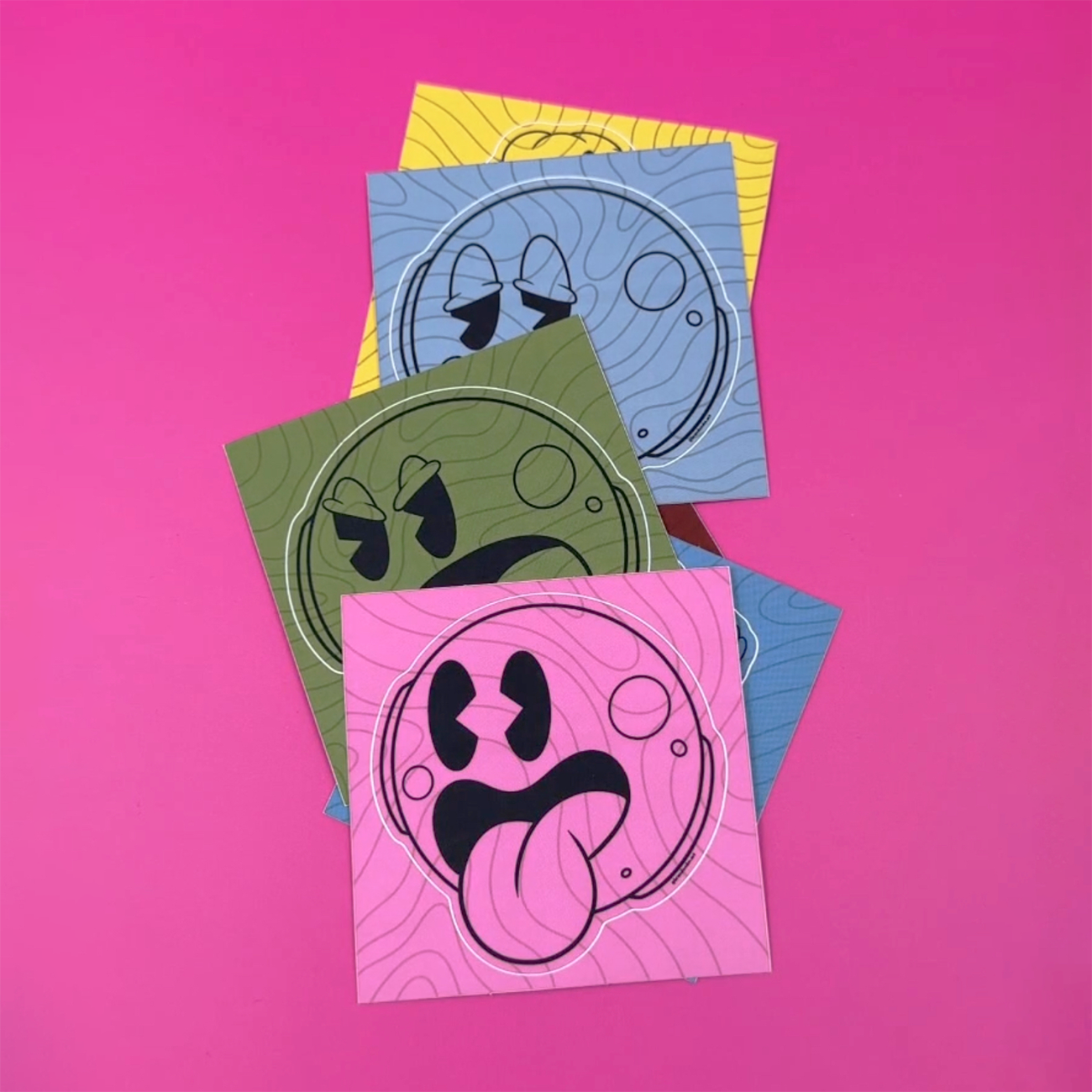 Kiss-cut sticker smiley ansigter i forskellige farver og ansigtsudtryk trykt på mat vinyl, mod en pink baggrund.