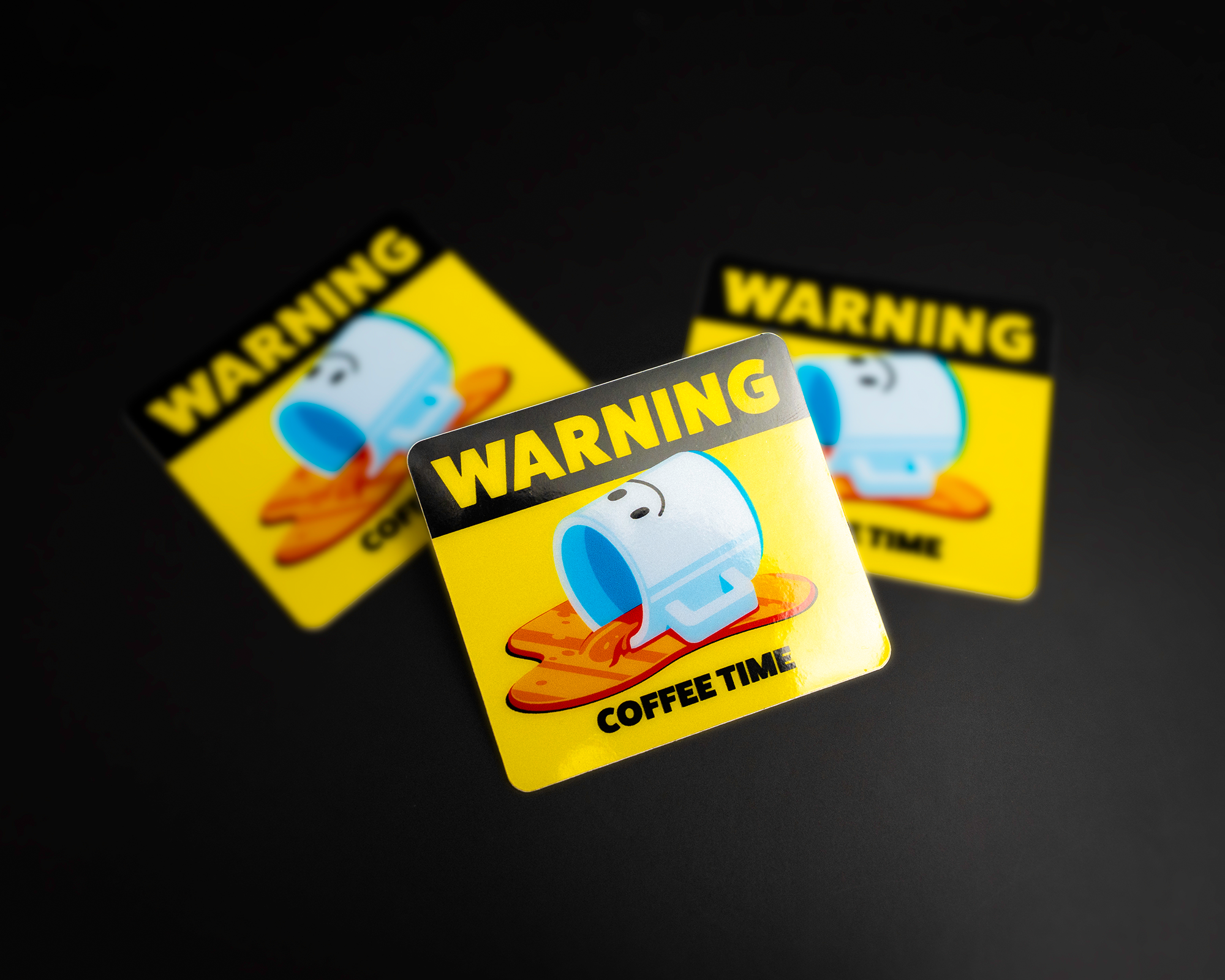 Three yellow stickers with a spilled coffee cup illustration and the text "WARNING COFFEE TIME" on a dark background.