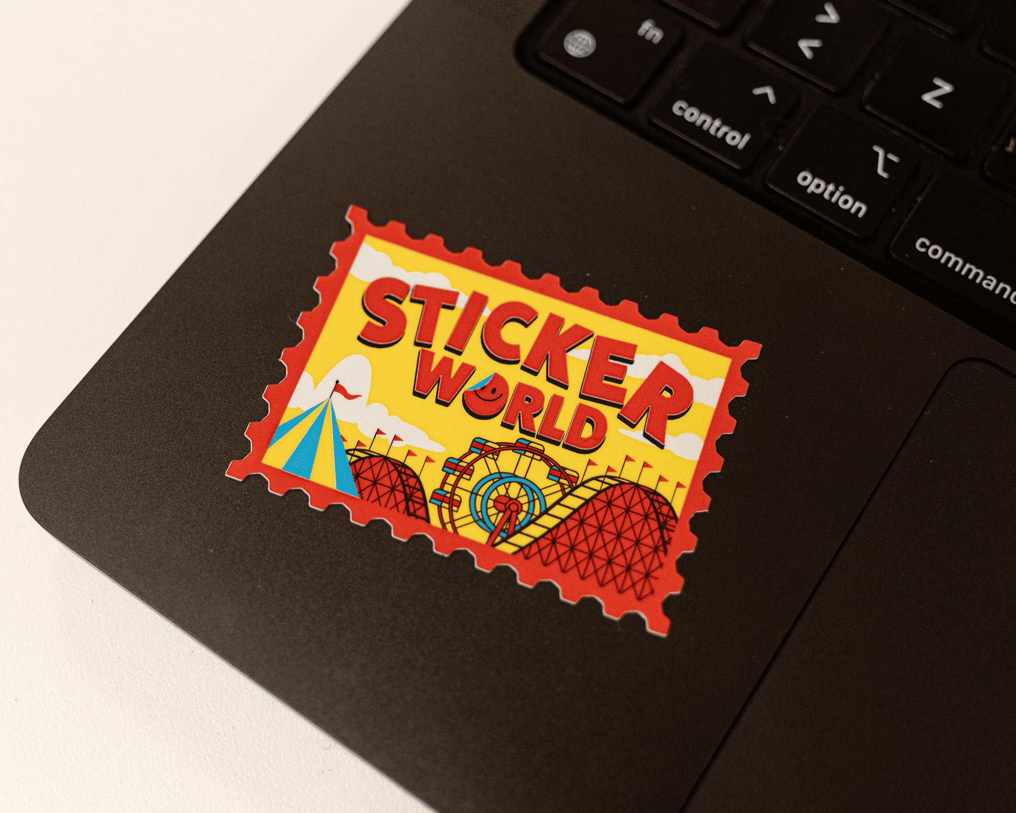 Colorful "Sticker World" sticker on a laptop, featuring amusement park rides and a tent in a red and yellow design.